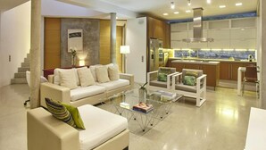 Ein modernes Wohnzimmer mit einer Couch, Sesseln und einem Couchtisch. Es gibt eine Küchenzeile mit einem Kühlschrank und einer Spüle.