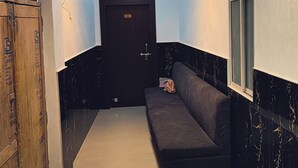 Un couloir avec un canapé de couleur sombre, une porte en bois portant l’inscription « HALL » et un lustre.