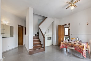 A spacious room with a wooden staircase, a dining table set with plates and glasses, and a ceiling fan.