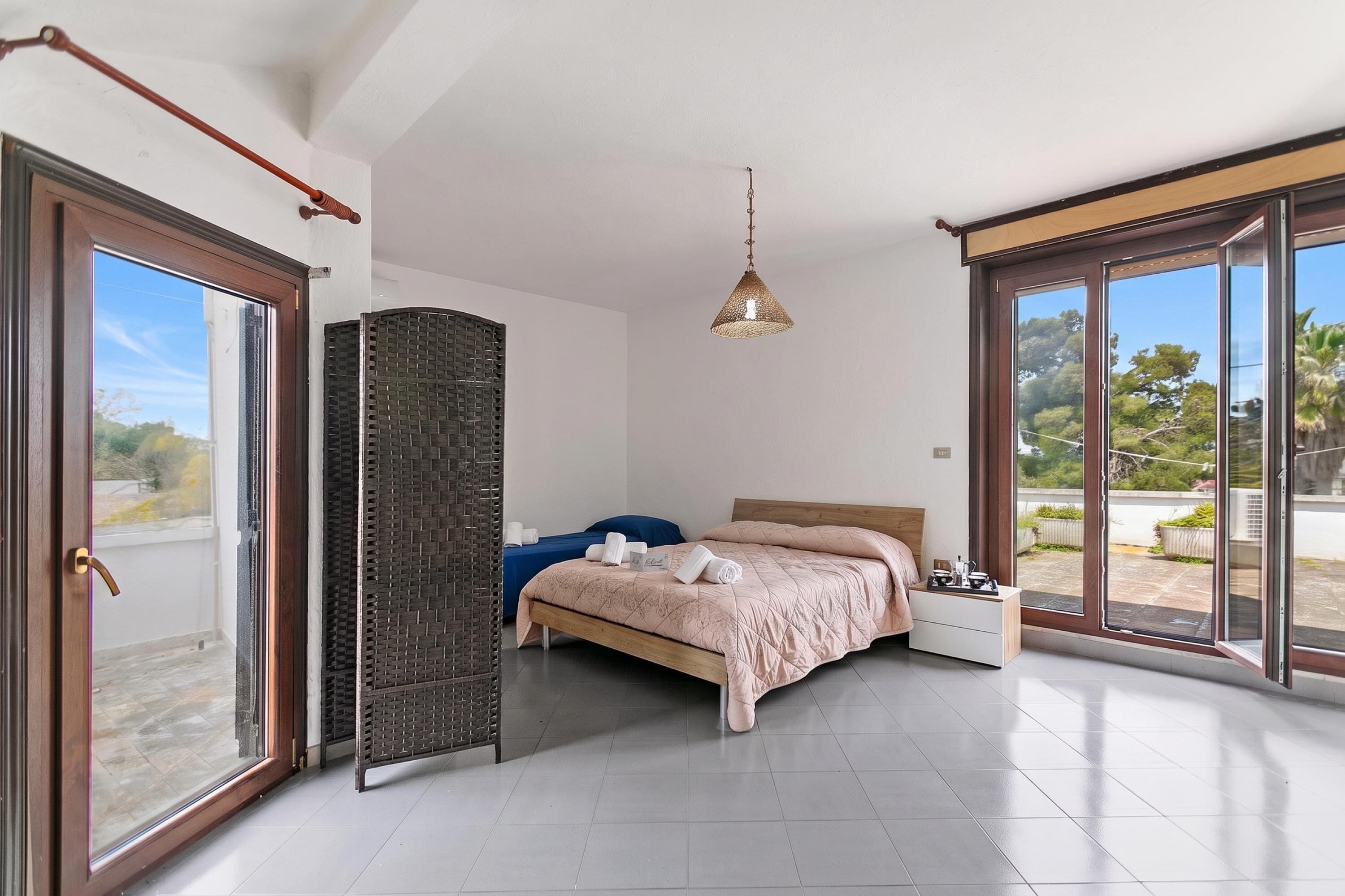 A bedroom with a bed, a nightstand, a hanging light, and a view through large glass doors.