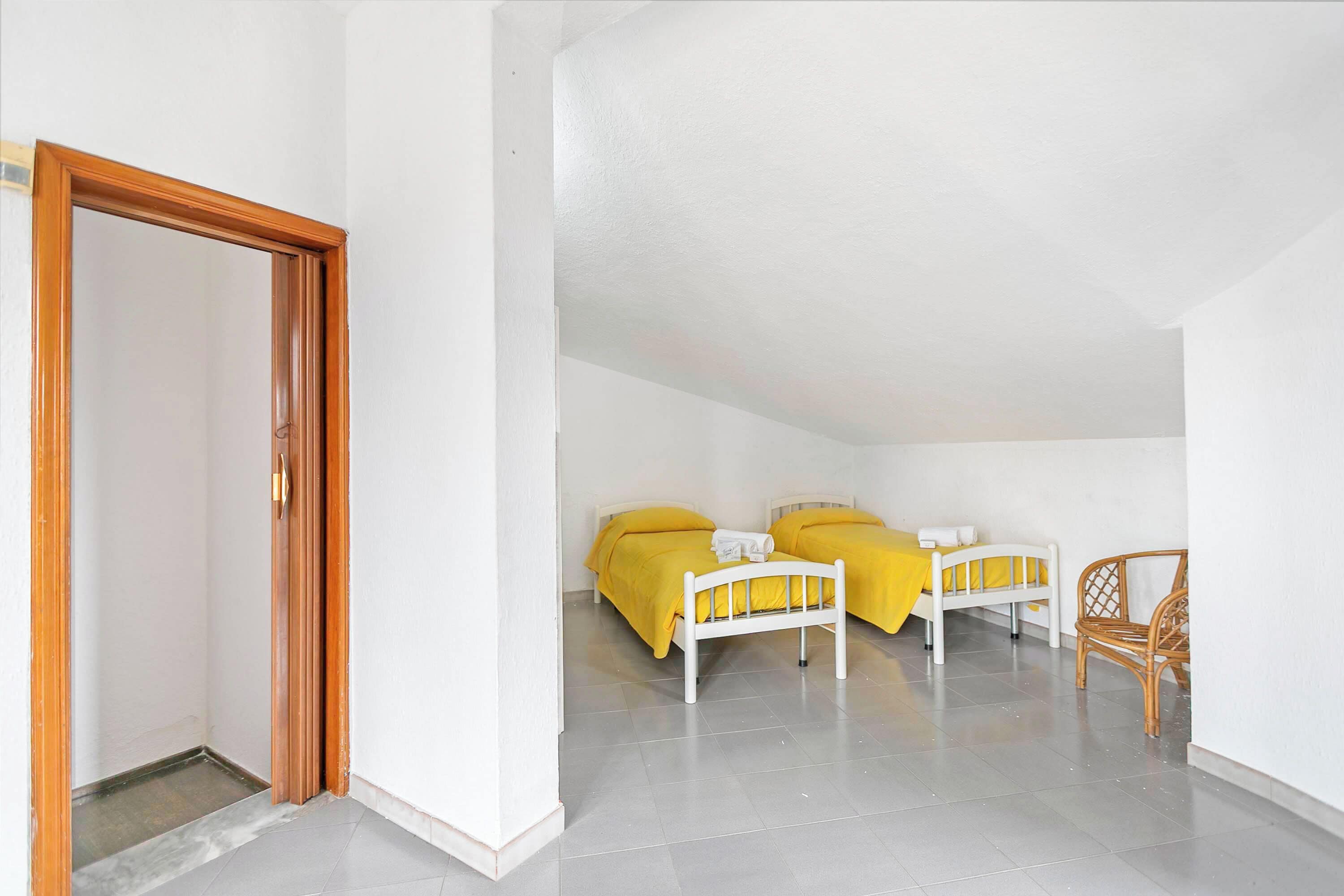 Une chambre avec deux lits, une porte en bois et une chaise en osier.