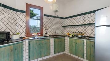 Uma cozinha com armários verdes, micro-ondas, torradeira, pia e janela com vista para árvores.