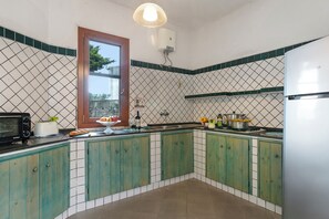 A kitchen with green cabinets, a microwave, a toaster, a sink, and a window with a view of trees.