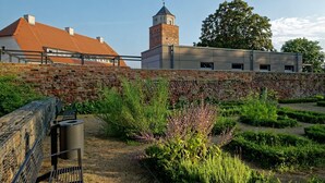 A courtyard with a brick wall, a building with a tower, and a garden with various plants. - Modern Suite in the Taunus (Bad Camberg)