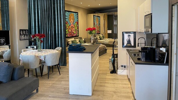 A modern living room with a sofa, a dining area with a table and chairs, a kitchen with a microwave and a TV, and a bedroom with a bed and curtains. - Modern Suite in the Taunus (Bad Camberg)