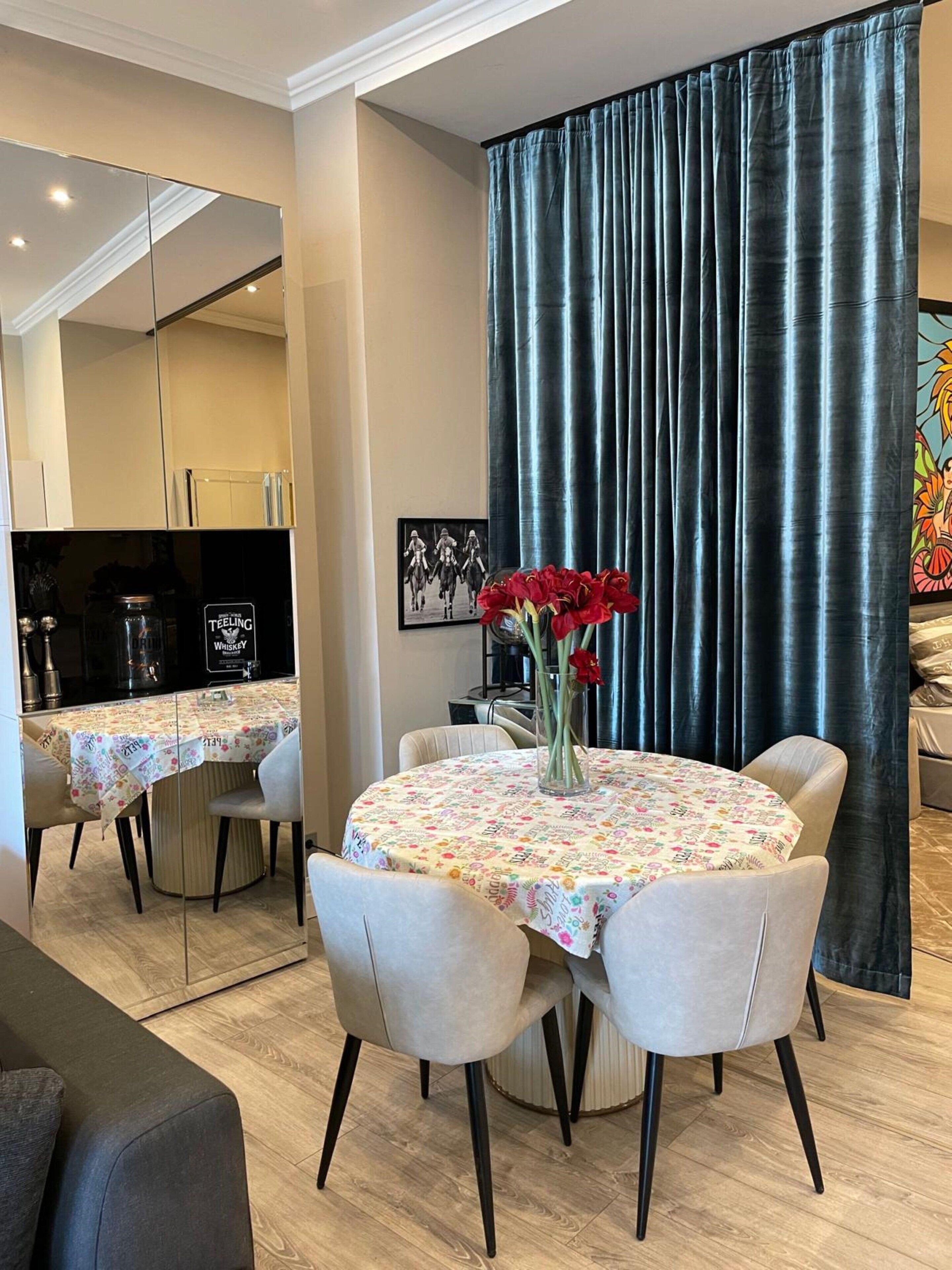 A modern dining area with a round table, four chairs, and a vase with red flowers.