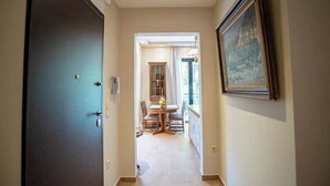A hallway leading to a dining area with a table and chairs, a dark door on the left, and a framed picture on the wall.