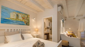 A hotel room with a bed, a sofa, a painting on the wall, and a bathroom visible through an open door. - Luxury Apartment Lina - I (Dubrovnik)