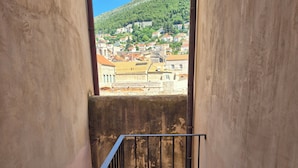 A narrow balcony with a metal railing, a view of a hillside town, and a stone wall. - Luxury Apartment Lina - I (Dubrovnik)