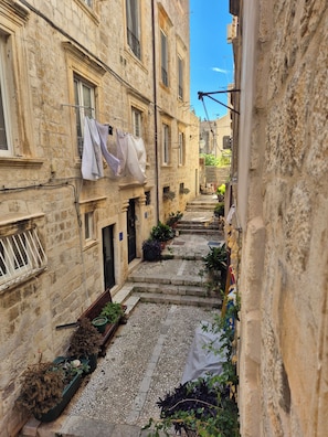 Une ruelle étroite bordée d’immeubles en pierre, une corde à linge tendue avec des vêtements et des plantes en pot.