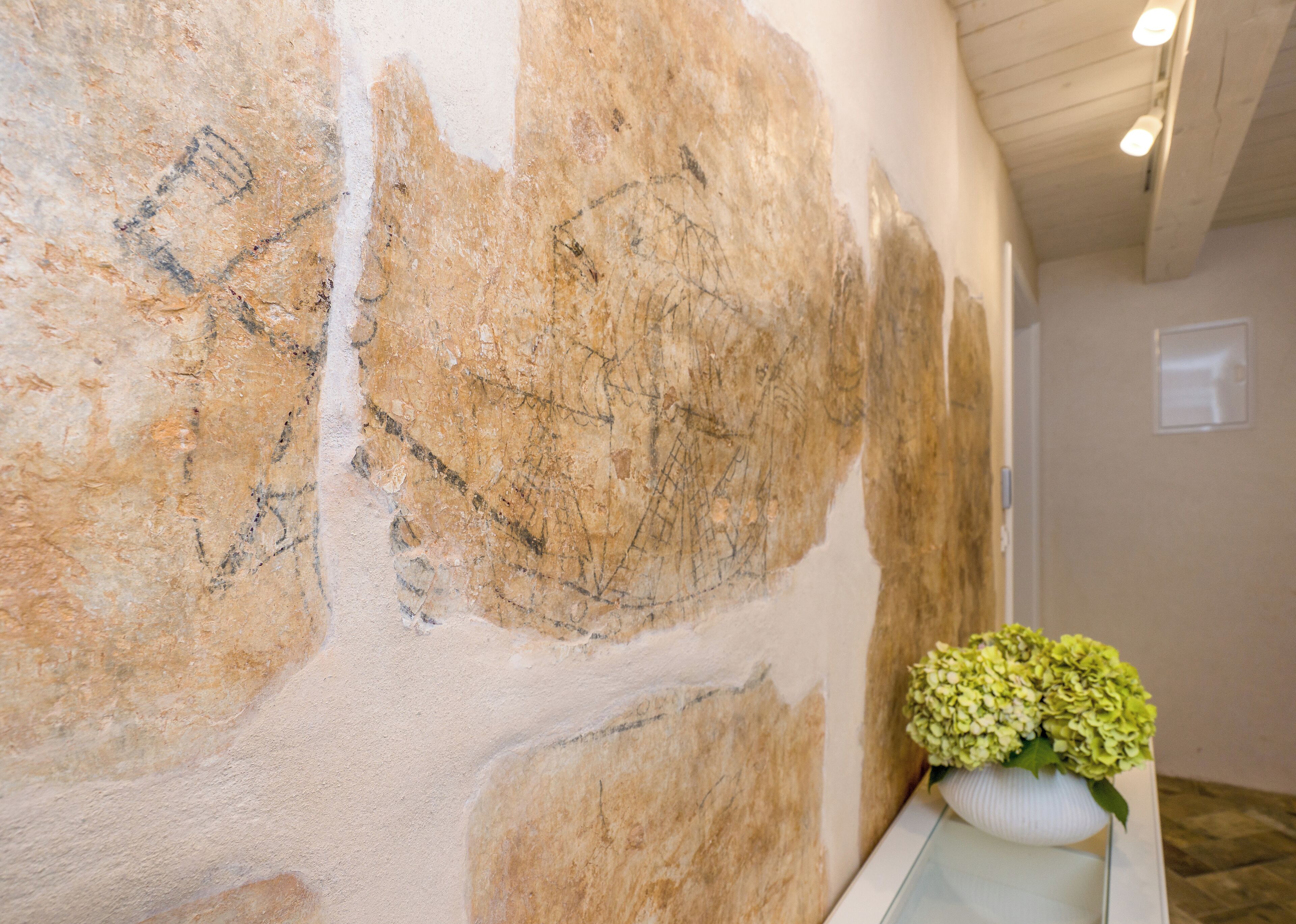 A stone wall with carvings, a white vase with green flowers, and a wooden ceiling.