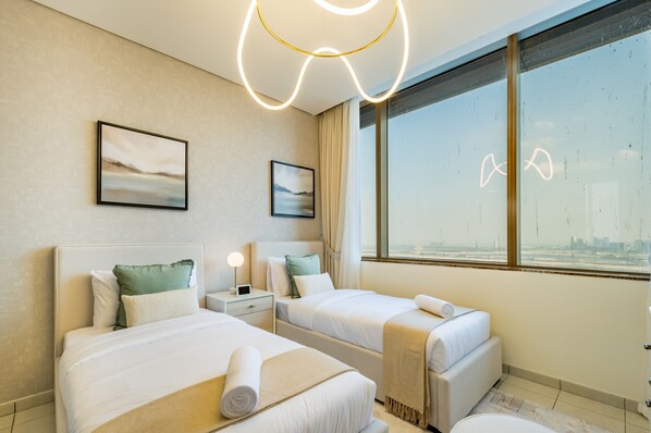 A hotel room with two beds, a nightstand, a lamp, and a large window with a city view.