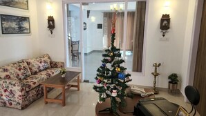 Una sala de estar con un sofá floral, una mesa de centro, un árbol de Navidad y un escritorio con un teléfono y un marco de fotos.