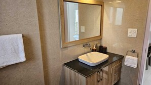 Un baño moderno con un espejo grande, un lavamanos blanco, armarios de madera y un perchero para toallas.