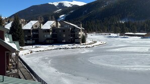 A multi-story building with balconies, a snow-covered mountain in the background, and a frozen river in the foreground. - Beautiful Renovated 1br Lakeside Condo 1 Bedroom Condo (Keystone)