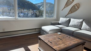 A modern living room with a large window, a grey sofa, and a wooden coffee table. - Beautiful Renovated 1br Lakeside Condo 1 Bedroom Condo (Keystone)