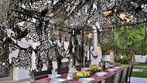 An outdoor dining area with a table set for four, surrounded by chairs, under a netted pergola. - Amazing Villa Near Ibiza Town (Santa Eulalia del Rio)
