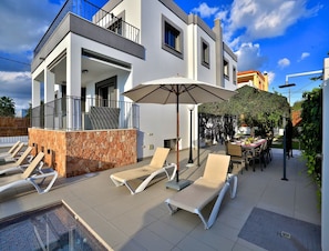 En moderne bygning med et poolområde, udendørs siddepladser og en overdækket terrasse.