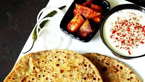 A plate of flatbreads, a bowl of yogurt with red spice, and a dish of cooked vegetables.
