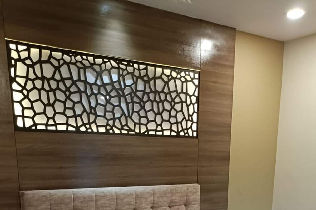A neatly made bed with a wooden headboard, a bedside table with a phone, and a decorative wall panel.