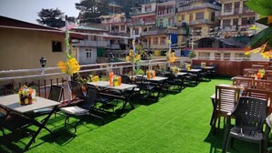 An outdoor seating area with tables and chairs, green artificial turf, and colorful decorations. - Hotel Akash - Luxury Hotel In Mcleodganj (Dharamshala)