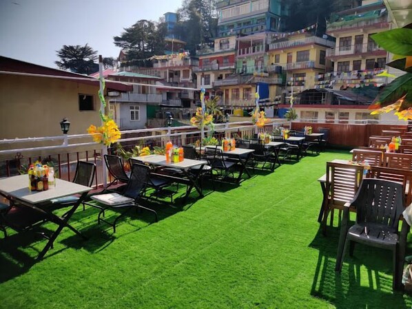 Un espacio al aire libre con mesas y sillas, césped artificial verde y decoraciones coloridas.