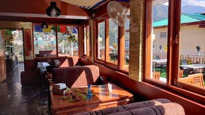 A cozy restaurant with wooden furniture, large windows, and a view of the mountains. - Hotel Akash - Luxury Hotel In Mcleodganj (Dharamshala)