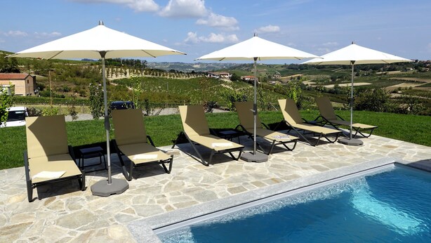 A poolside area with lounge chairs and umbrellas, a stone pool, and a scenic view of vineyards in the background. - Ultra-luxurious 6-bedroom villa with AC, WiFi in marvelous Piemonte (Piemonte)