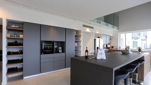 A modern kitchen with grey cabinetry, a central island with bar stools, wine bottles, and a large window providing natural light. - Ultra-luxurious 6-bedroom villa with AC, WiFi in marvelous Piemonte (Piemonte)