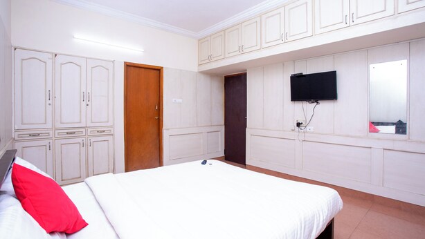 Een slaapkamer met een bed, een aan de muur bevestigde televisie en een kledingkast.