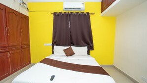 Een bed met een afstandsbediening, bruine gordijnen en een witte muur met een airconditioner.