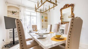Un comedor con una mesa de mármol, sillas blancas y una araña.
