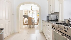 Una cocina moderna con muebles blancos, una estufa de acero inoxidable y un comedor con candelabro.