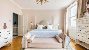 Un dormitorio con una cama grande, un chaise lounge, un tocador y una araña.