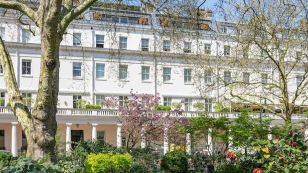 Un edificio de varios pisos con fachada blanca, ventanas amplias y un jardín con diversas plantas y flores.