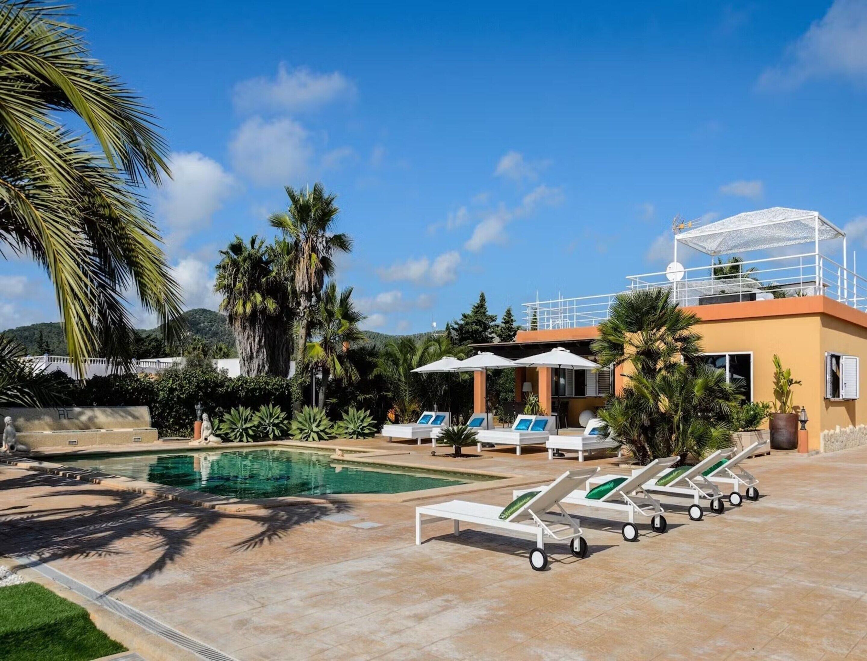 A pool area with lounge chairs, umbrellas, and a building with a balcony.