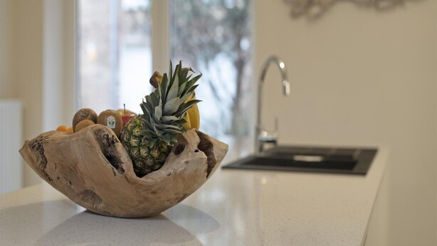 Un comptoir de cuisine avec un saladier en bois contenant des fruits et une bouteille.