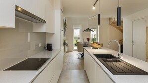 Une cuisine moderne avec des meubles blancs, un îlot central doté d’un évier et une plaque de cuisson à induction noire.