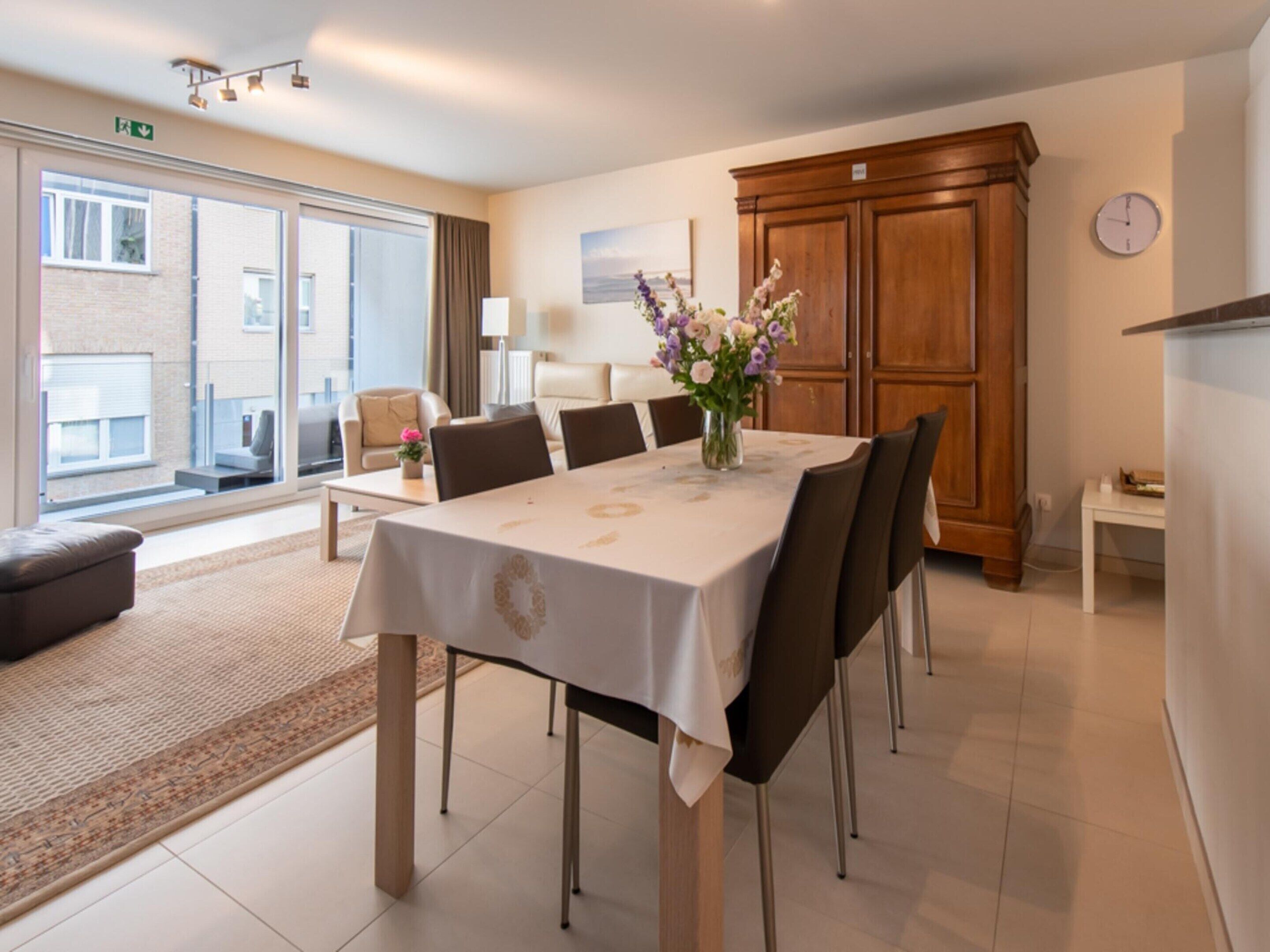 Een eetgedeelte met een tafel voor zes personen, een bloevas en uitzicht op buiten door een glazen deur.