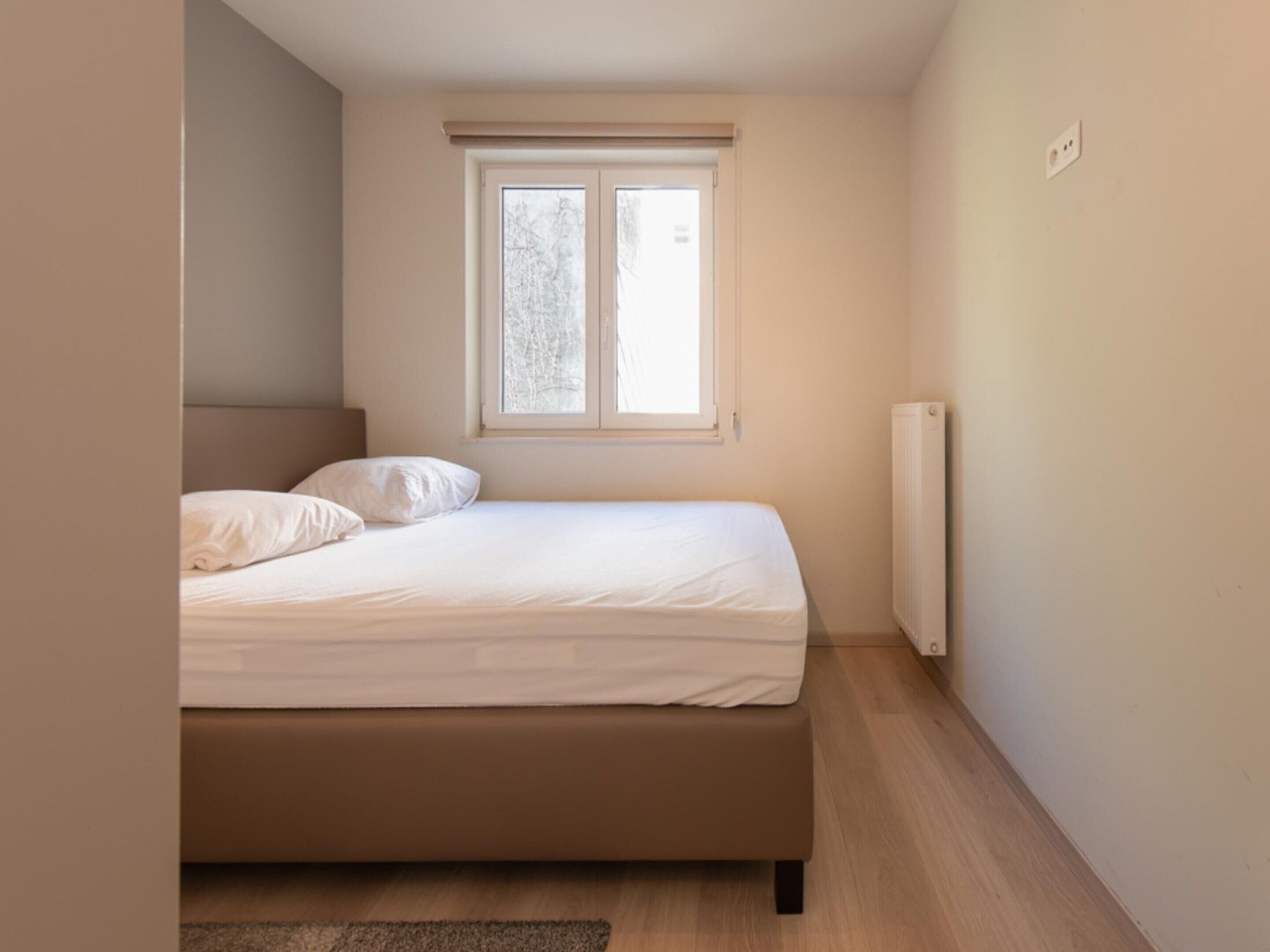 A bedroom with a bed, a radiator, and a window with a view of trees.