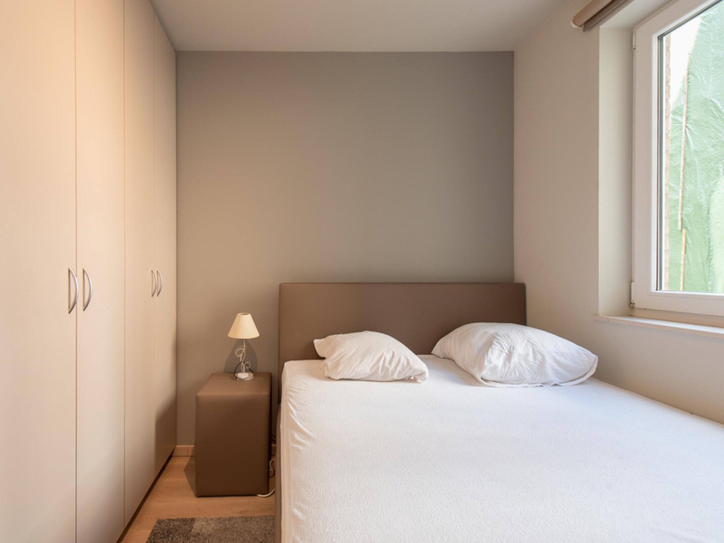 A bedroom with a bed, a nightstand, a lamp, and a wardrobe.