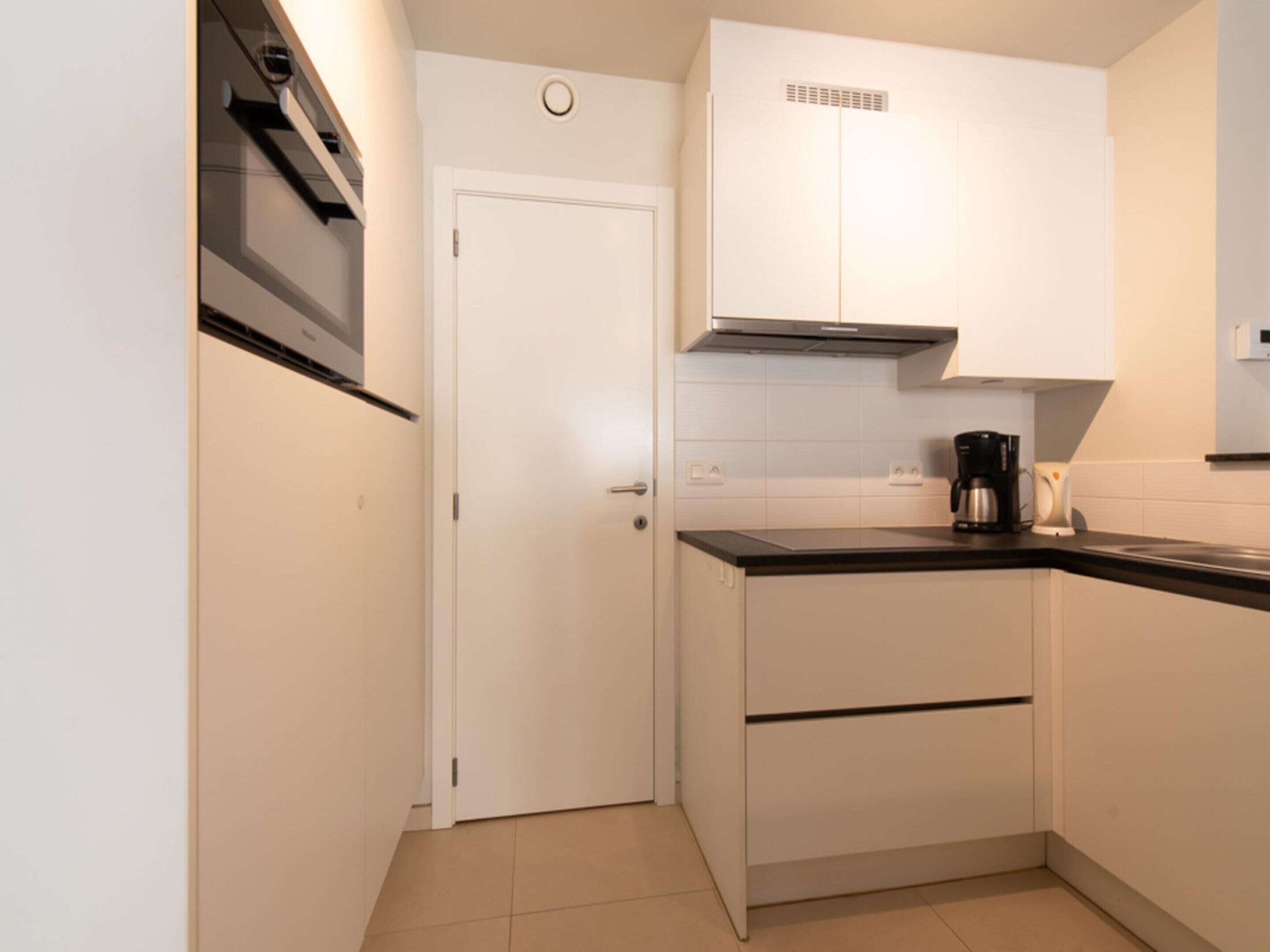A compact kitchen with white cabinets, a black countertop, and a white door.