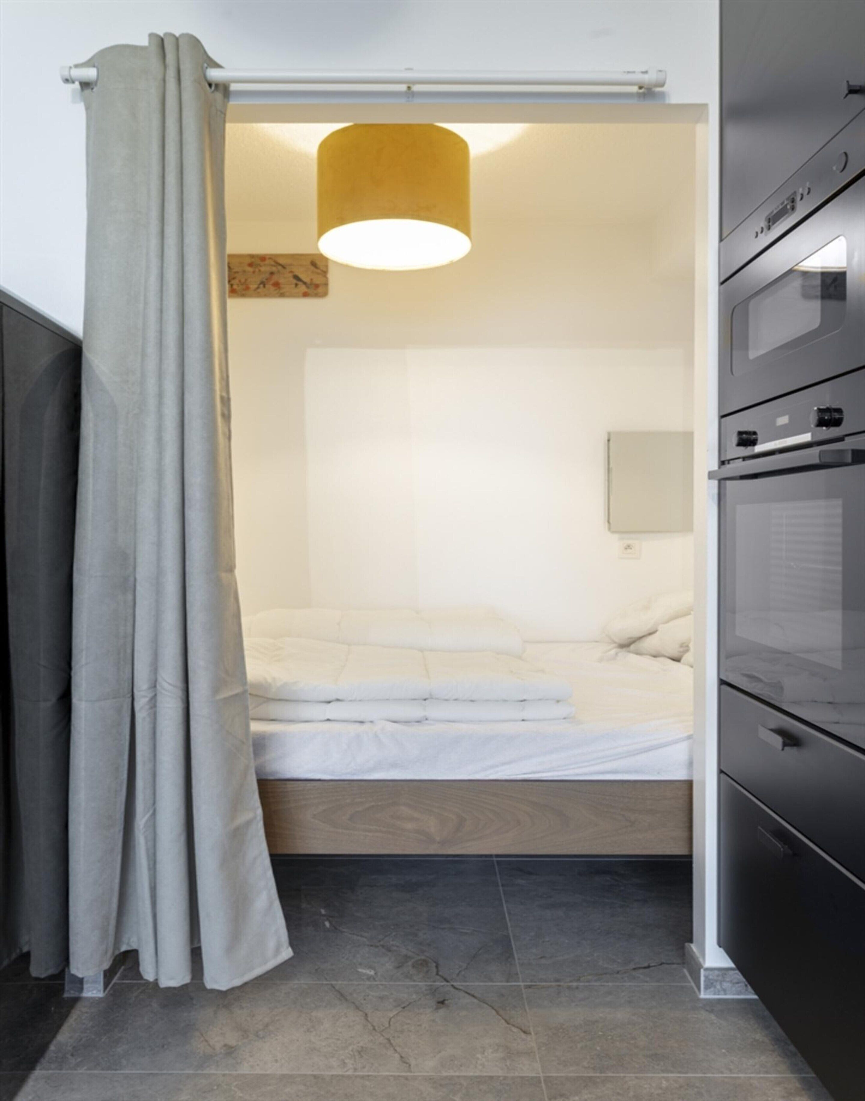 A compact bedroom with a bed, a ceiling light, and a built-in oven.