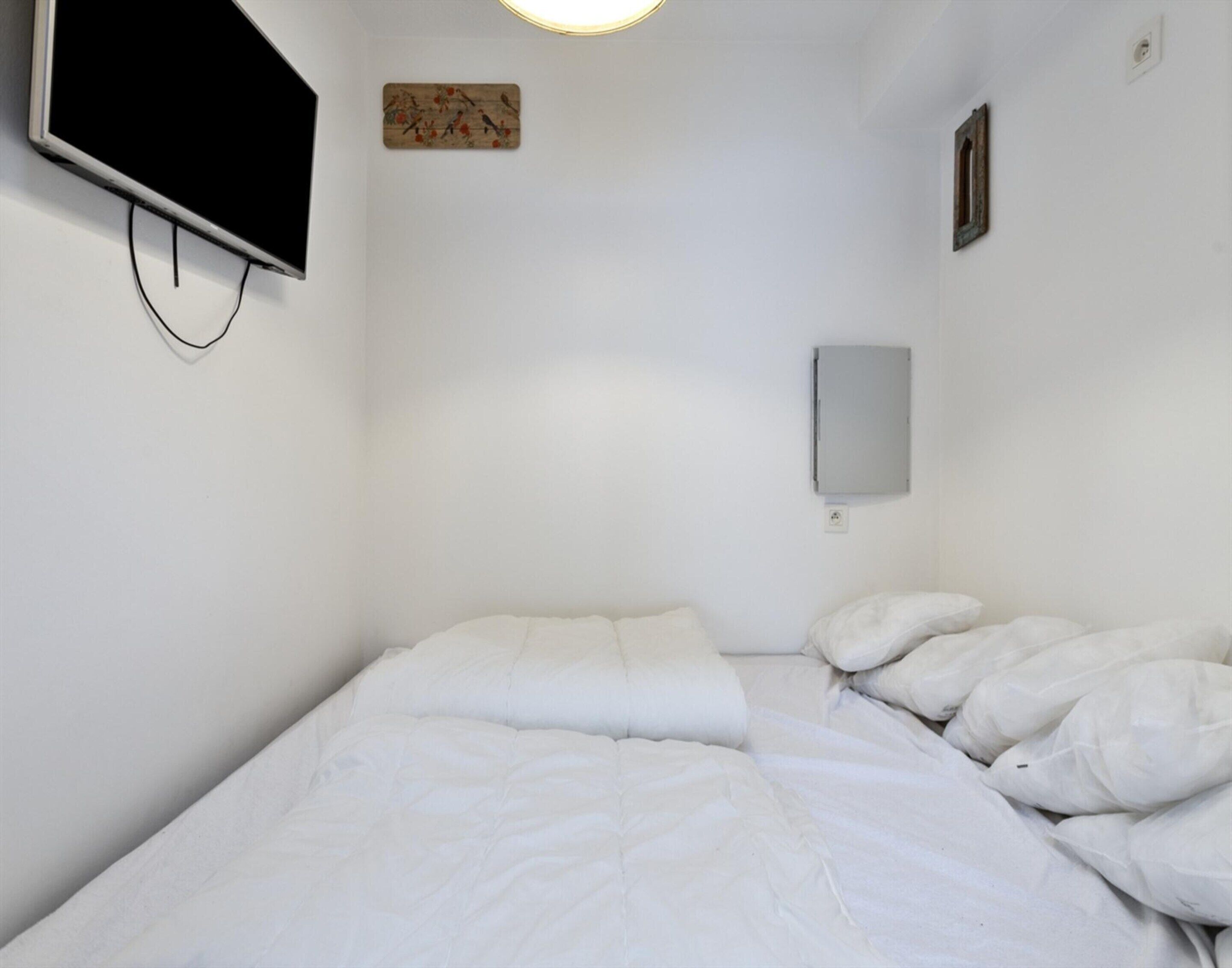 A simple, clean room with a bed, a flat-screen TV mounted on the wall, and a small electrical box.
