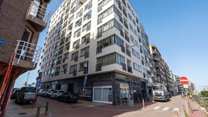 Een meerlaags woongebouw met balkons, een winkel op de begane grond en een parkeerplaats.