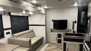 Cocina compacta para autocaravana con televisión integrada, zona de estar y una pequeña mesa de comedor.