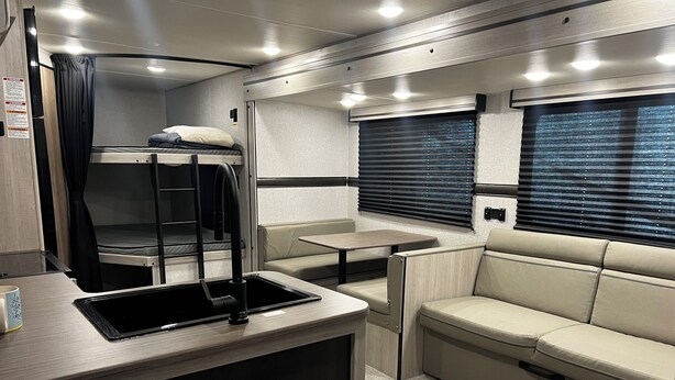 Interior compacto de una autocaravana con una litera, una zona de comedor y un área de estar.