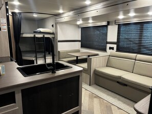 A compact RV interior with a bunk bed, a dining area, and a seating area. - Travel Trailer With a Lake View: Your Cozy Escape Awaits! (Bridgeport)
