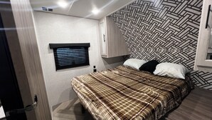 Un dormitorio con cama, ventana con persianas, pared con diseño y una puerta.