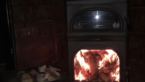 A wood-burning stove with a fire inside, set against a brick wall. - GOLDEN ELİT OTEL (Bandirma)